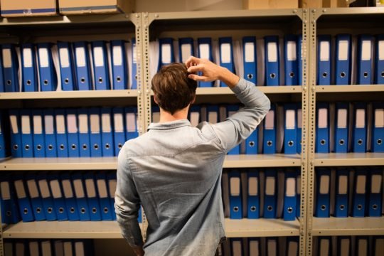 Rear view of confused businessman searching for files on cabinet in storage room