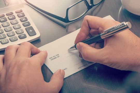 Man writing a payment cheque at the table with calculator and glasses